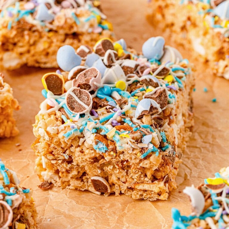 A rice crispy treat topped with colorful candy and chocolate pieces on parchment paper.