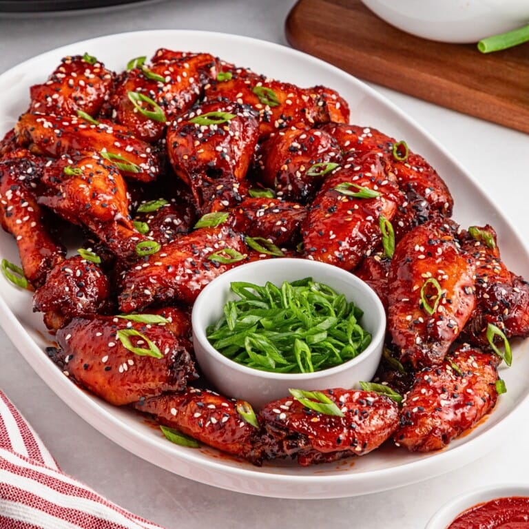 Plate of glazed chicken wings topped with sesame seeds and green onions.