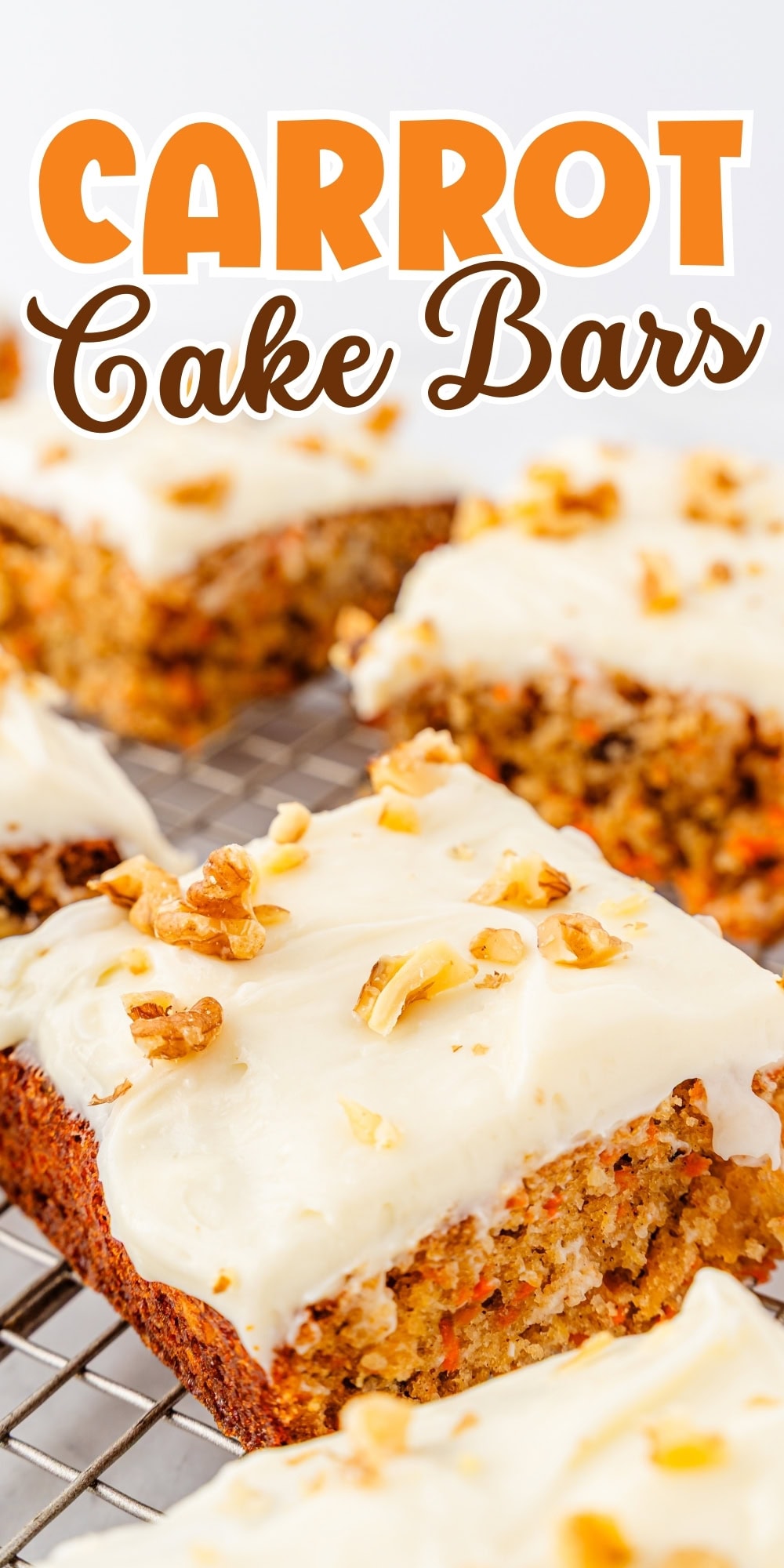 Carrot cake bars with cream cheese frosting and chopped walnuts on a cooling rack.