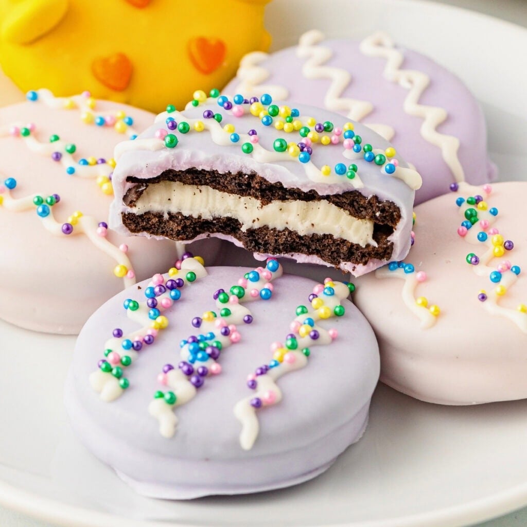 Chocolate sandwich cookies coated in pastel icing, decorated with colorful sprinkles.