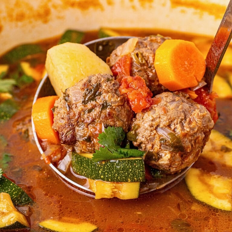 Ladle with meatballs, carrots, zucchini, and potatoes in tomato broth.