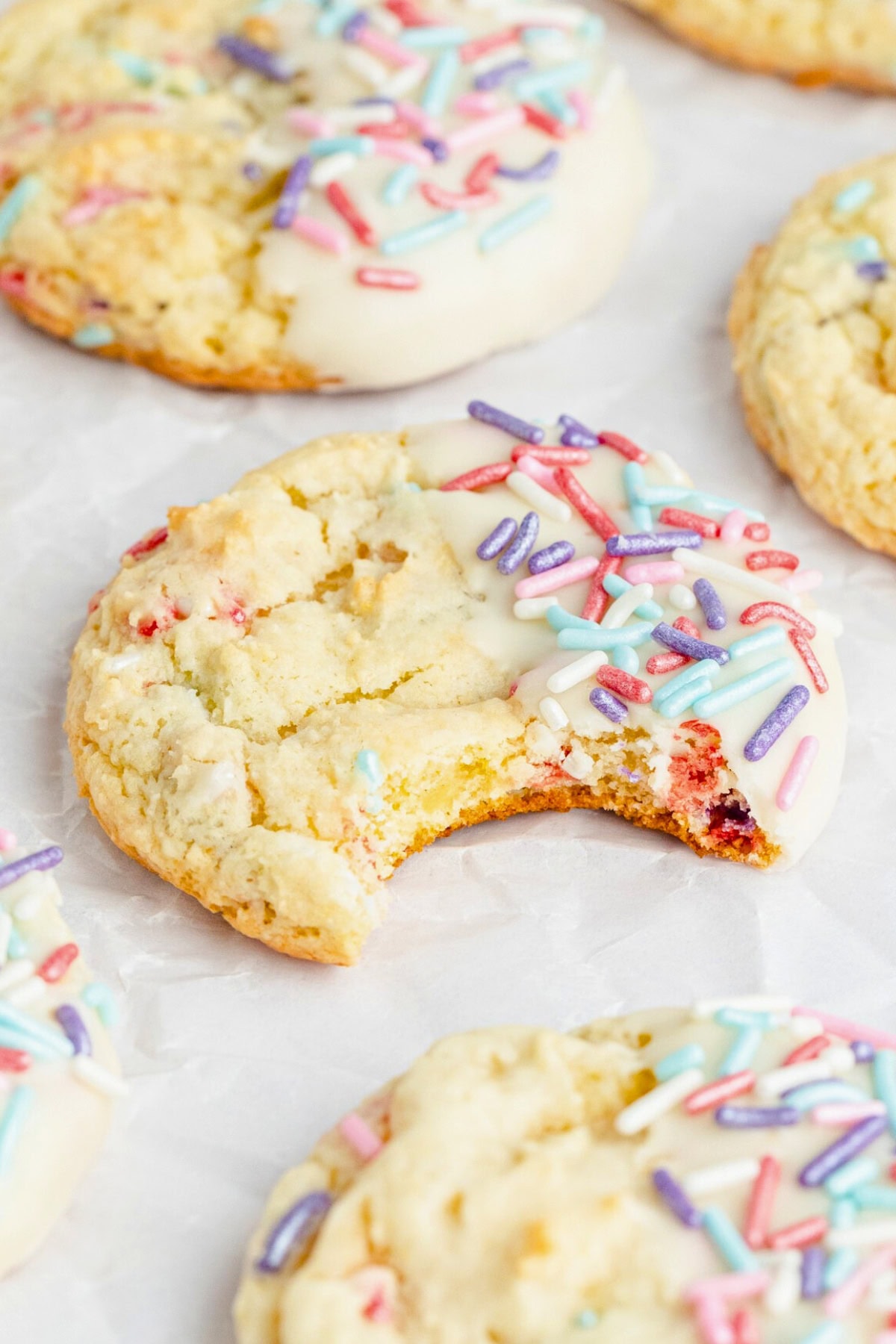 A cookie with colorful sprinkles and a bite taken out, on parchment paper.