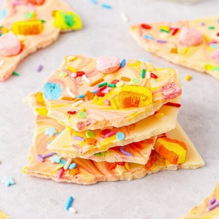 Colorful candy bark pieces topped with sprinkles and marshmallows on a white surface.
