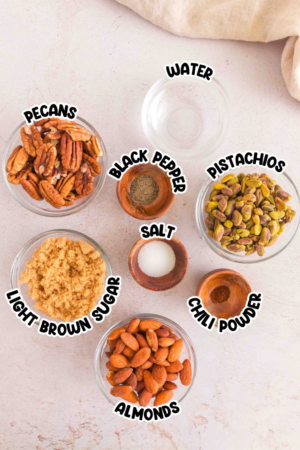 Bowls of pecans, pistachios, almonds, brown sugar, spices, and water on a table.