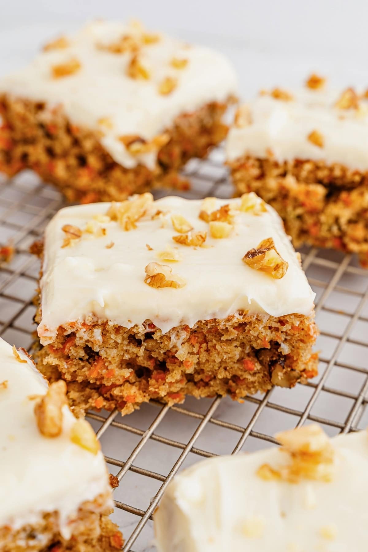 Carrot cake bars with cream cheese frosting and chopped walnuts on a cooling rack.