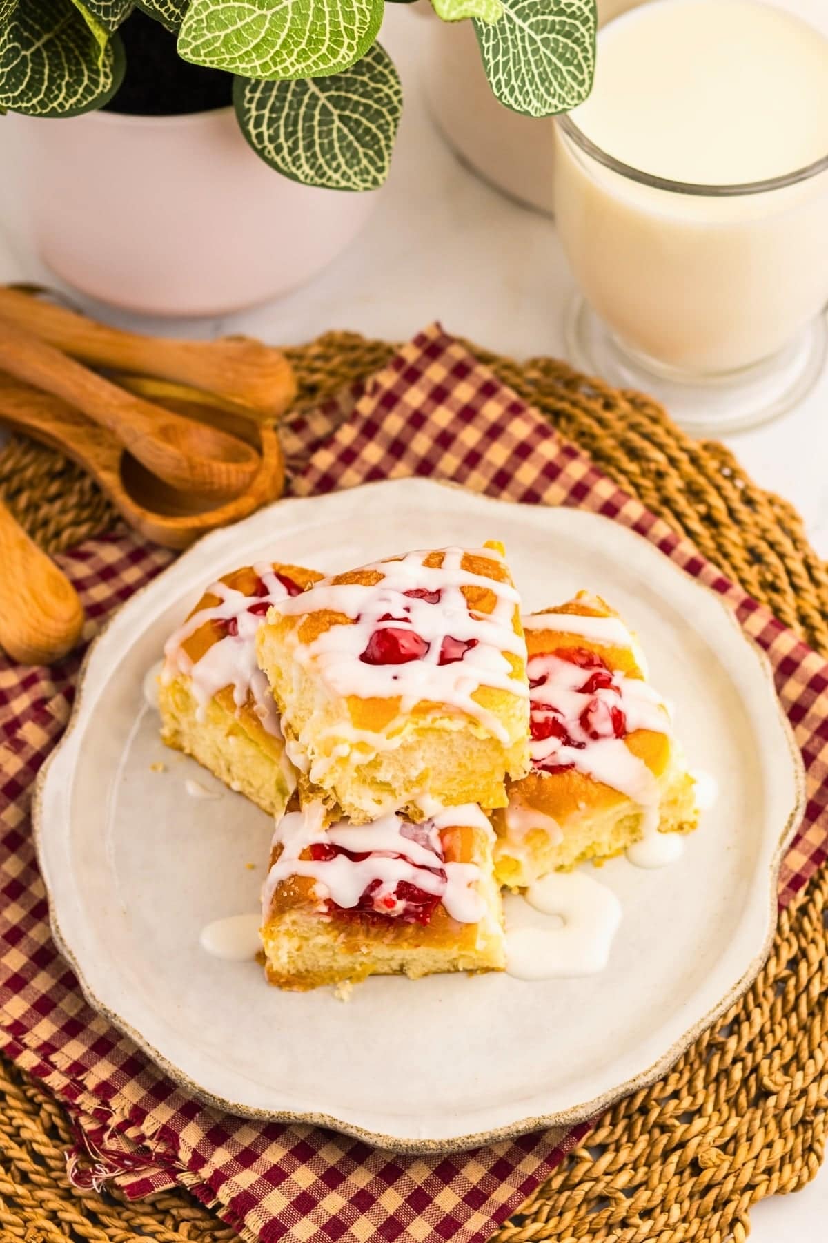 Four glazed cherry bars on a plate with a glass of milk and wooden utensils.