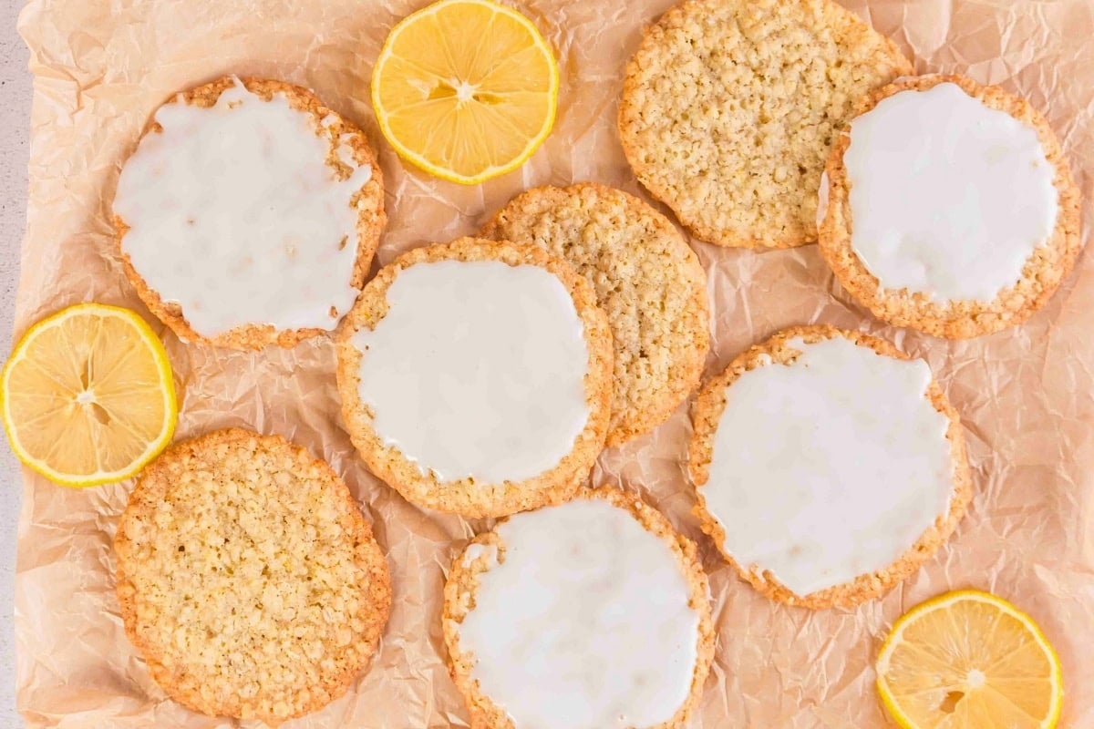 Oatmeal cookies with white icing and lemon slices on parchment paper.