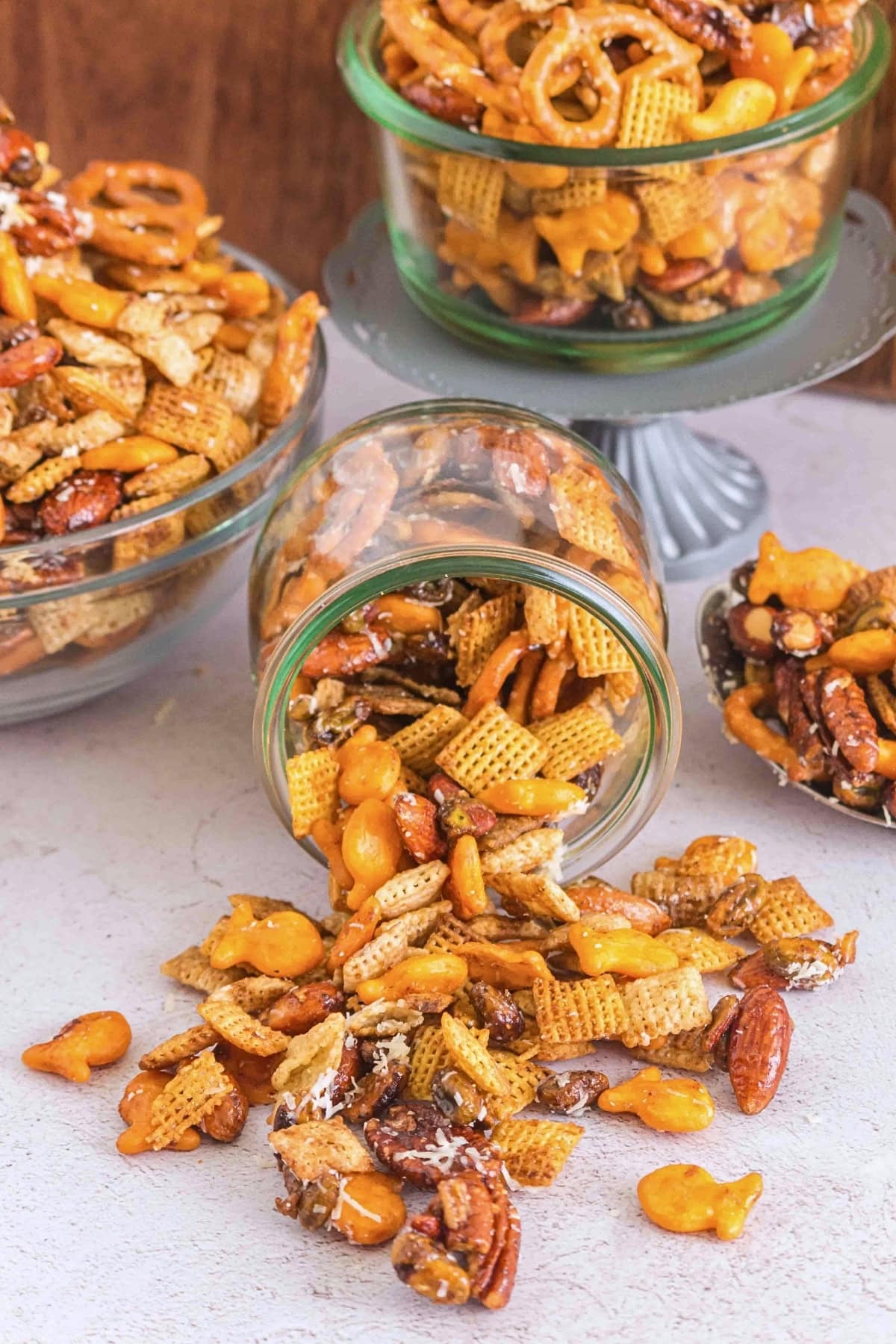Snack mix with pretzels, cereal, nuts, and crackers spilling from a glass jar.