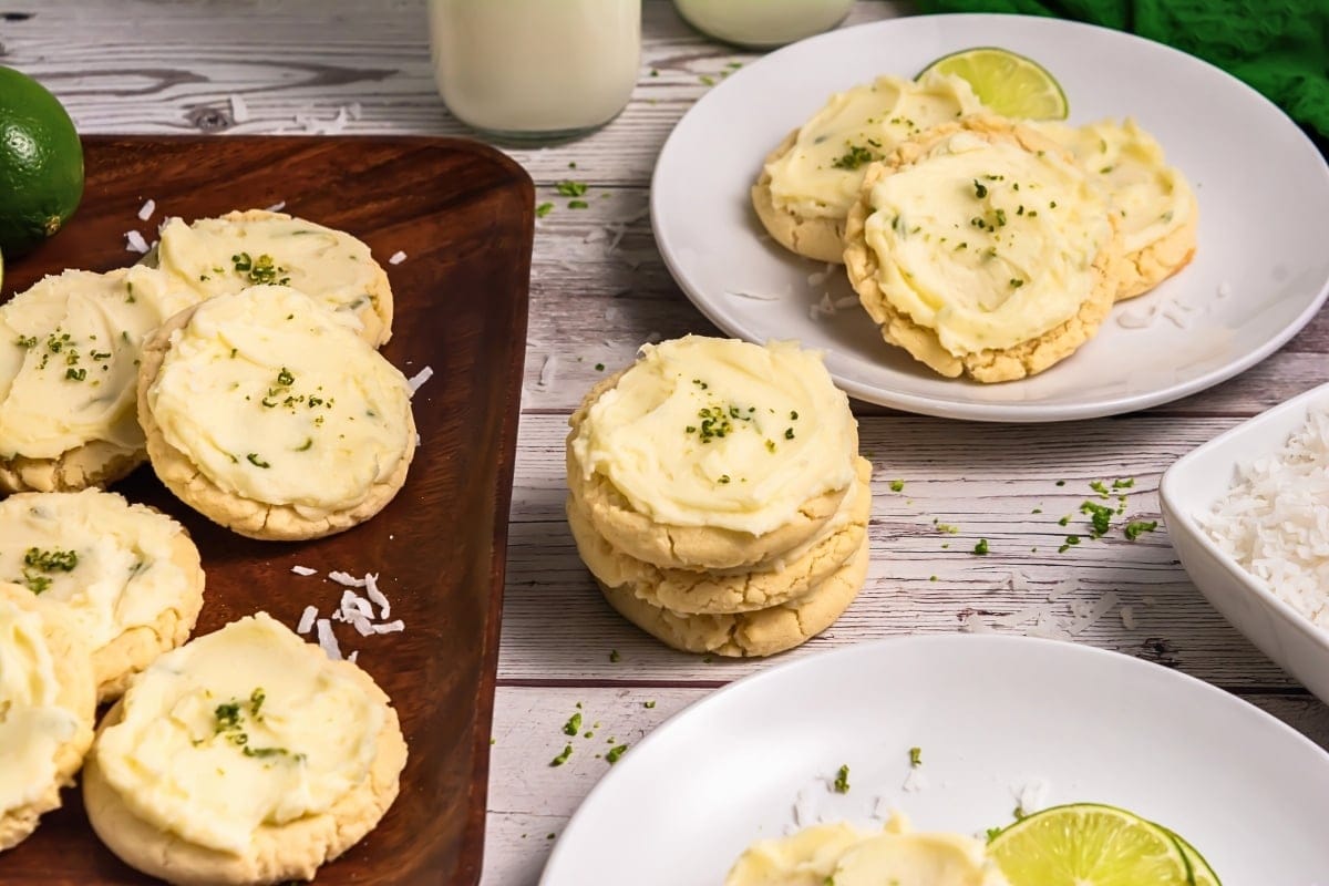 Sugar cookies with white frosting and lime zest on plates and a wooden tray.