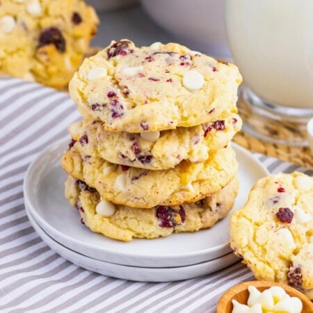 A stack of white chocolate cranberry cookies on a plate next to a glass of milk.