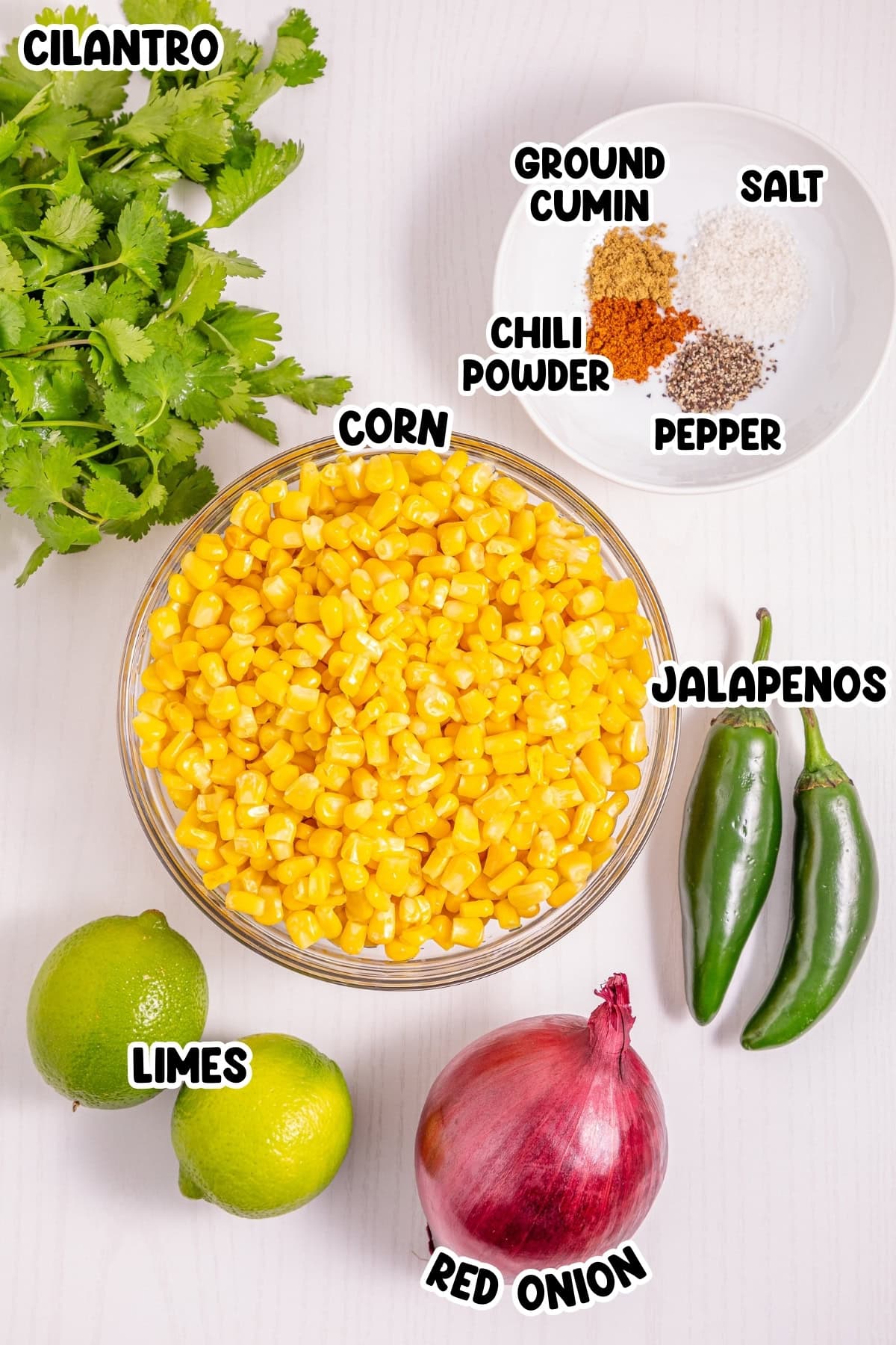 Bowl of corn, cilantro, limes, jalapenos, red onion, and spices on a table.