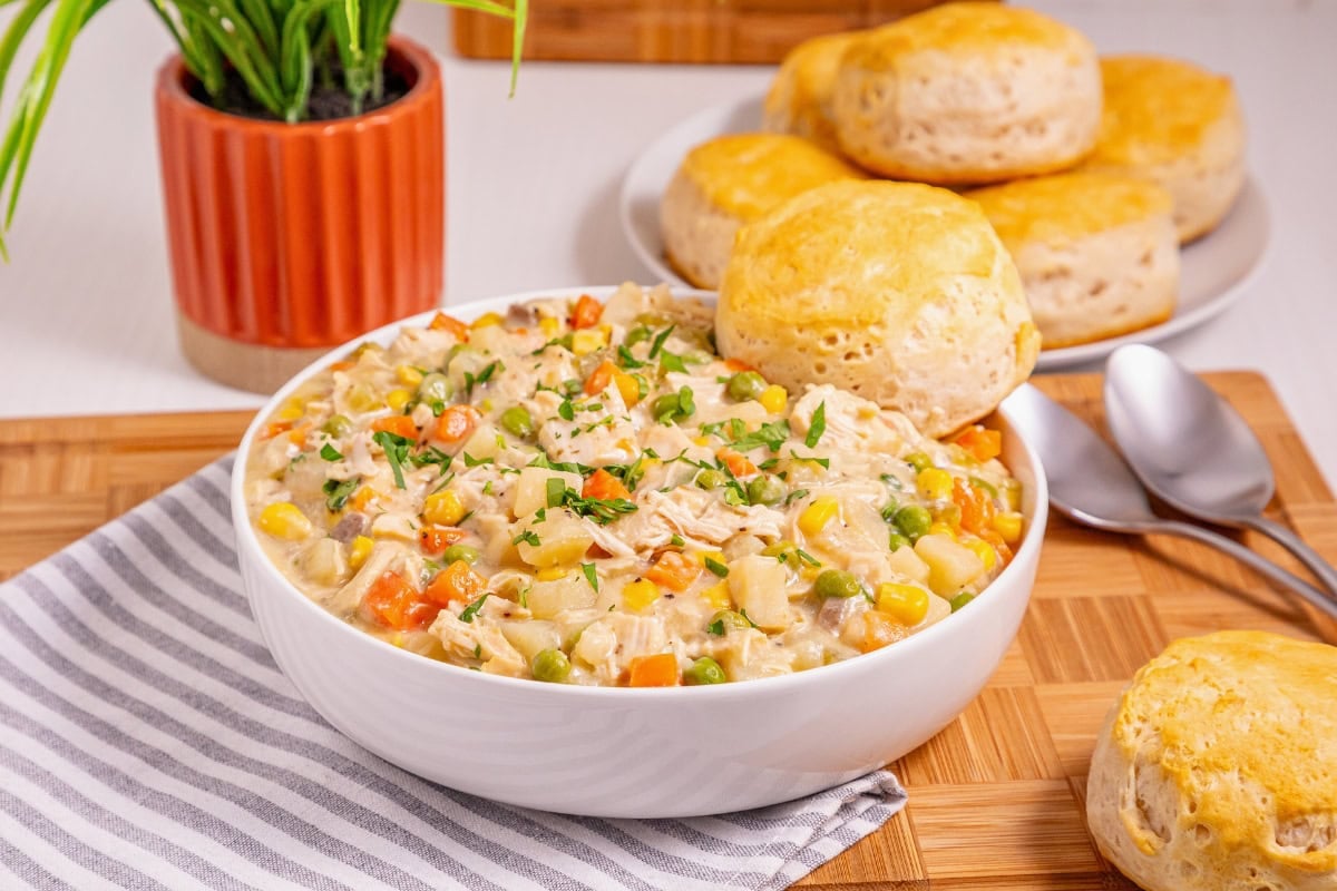 A bowl of creamy chicken and vegetable with biscuits on the side.