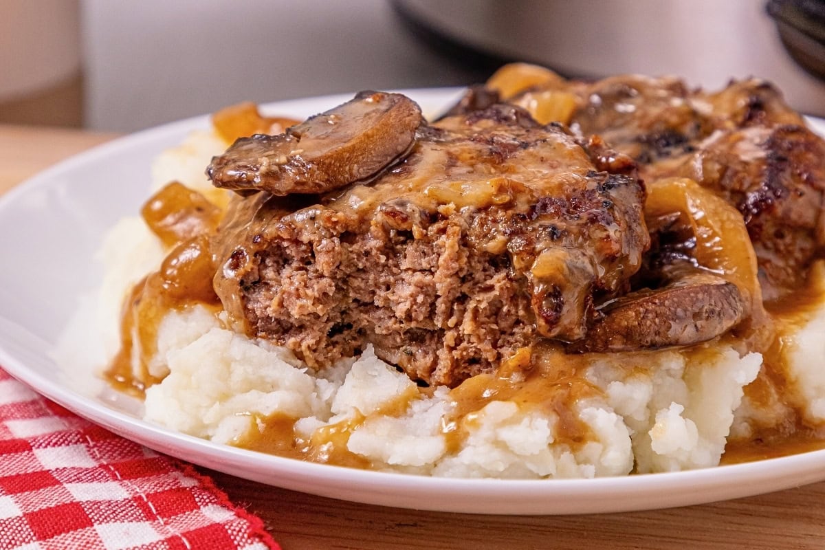 Salisbury steak with gravy and mushrooms on mashed potatoes, bite taken out.