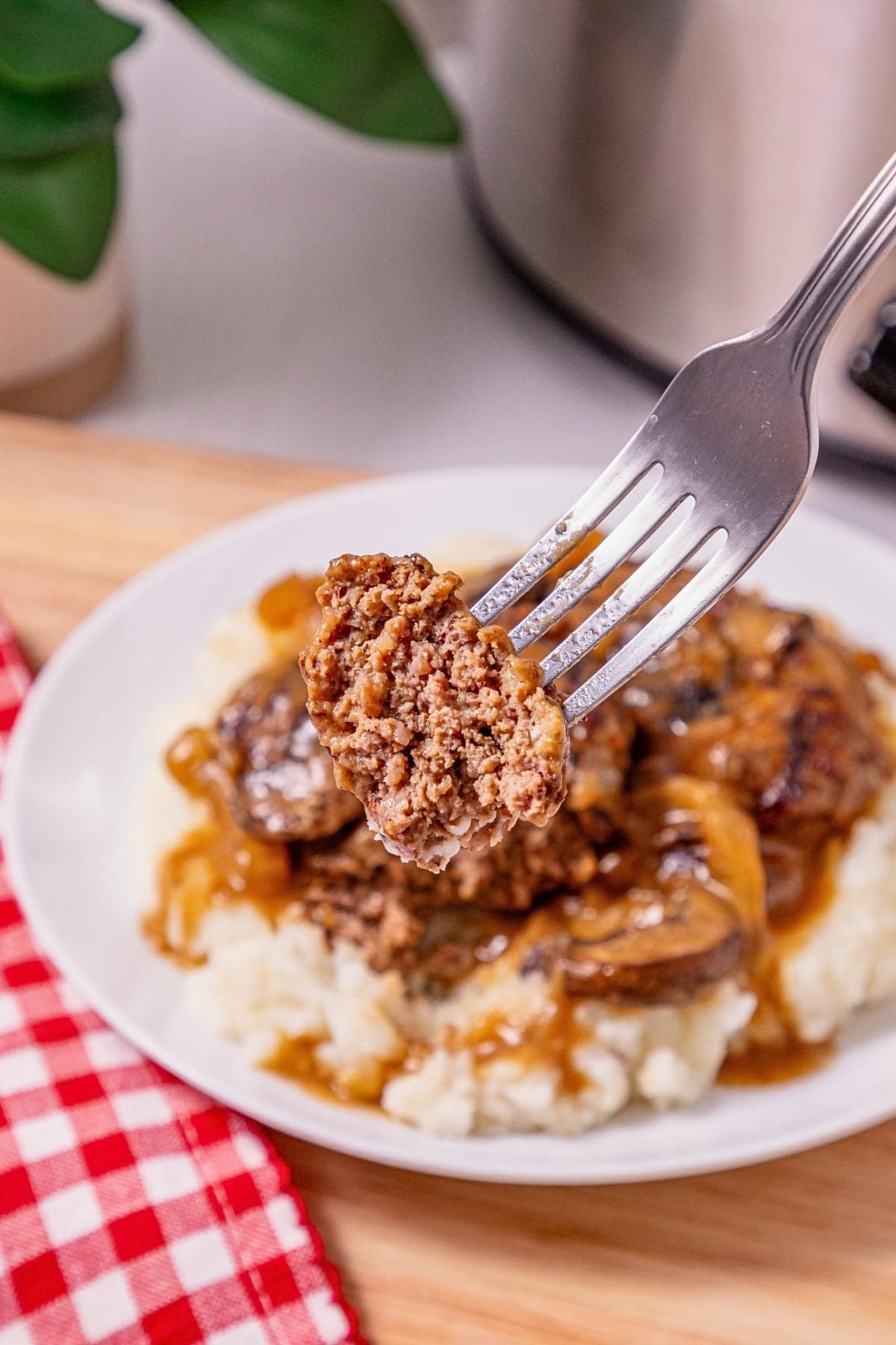 A fork holds a bite of Salisbury steak over mashed potatoes with gravy.
