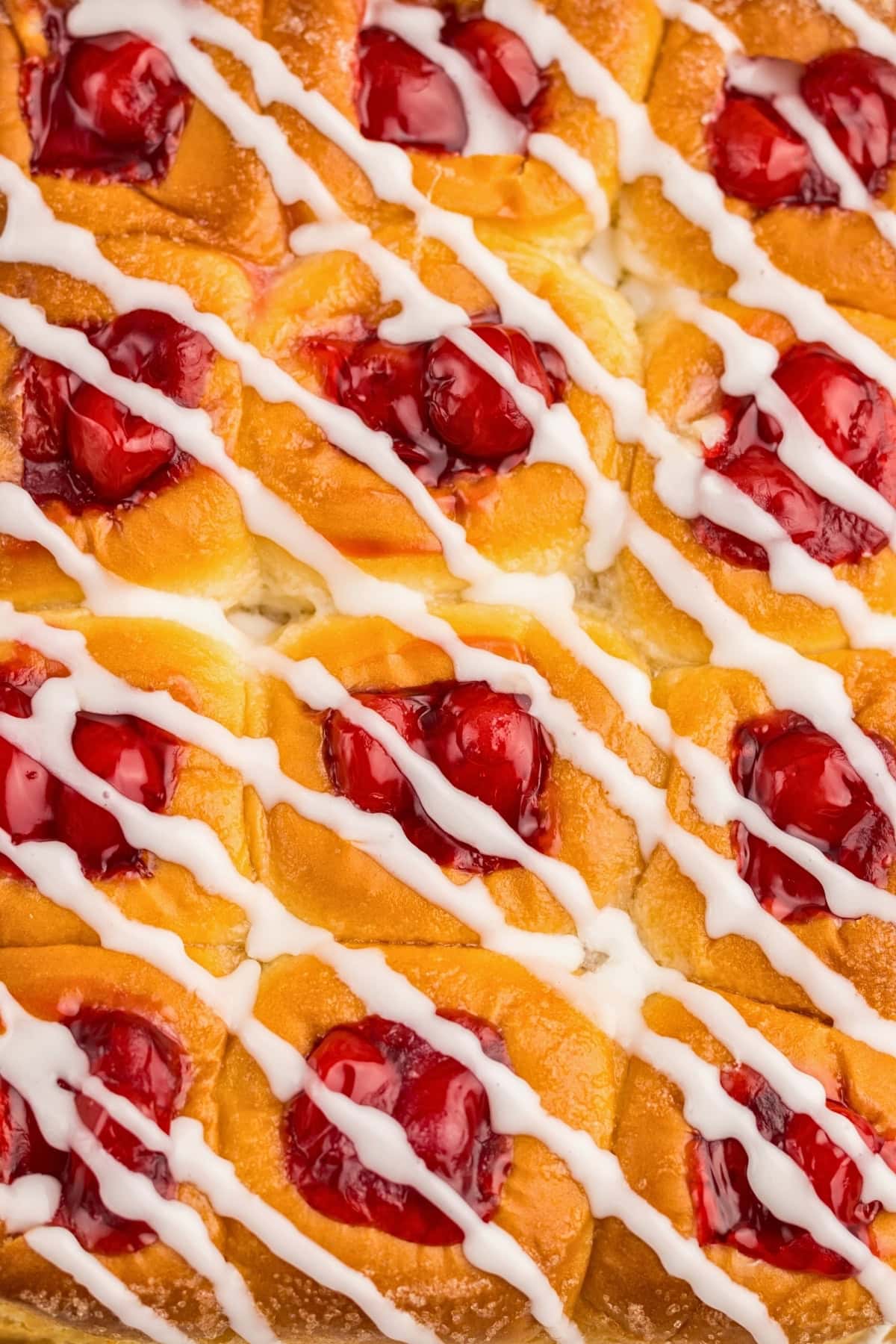 Cherry danish pastry with icing drizzled in diagonal lines across the top.