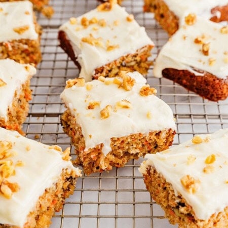 Carrot cake bars with cream cheese frosting and chopped walnuts on a cooling rack.