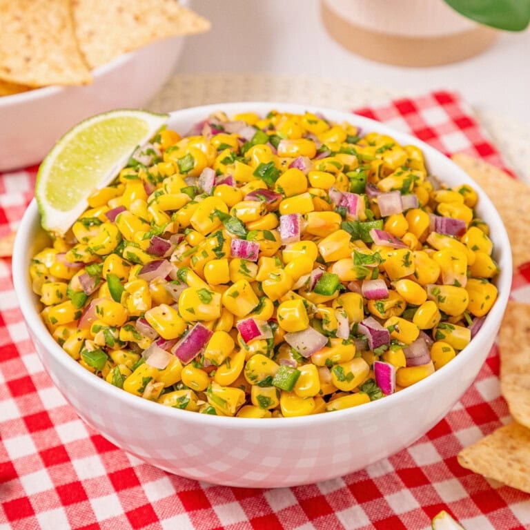 A bowl of corn salad with red onions, herbs, and a lime wedge on the side.