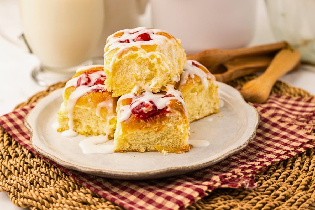 Three cherry sweet rolls with icing stacked on a plate, on a woven placemat.