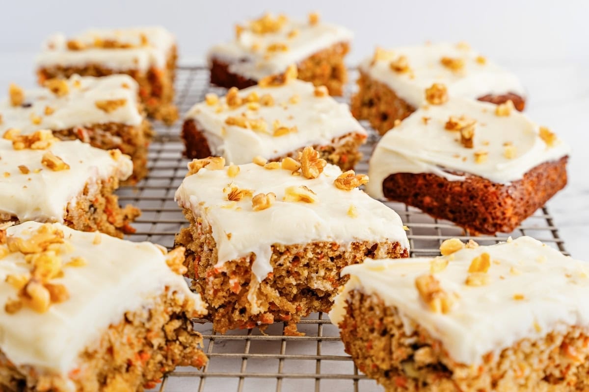 Frosted carrot cake bars topped with chopped walnuts on a cooling rack.