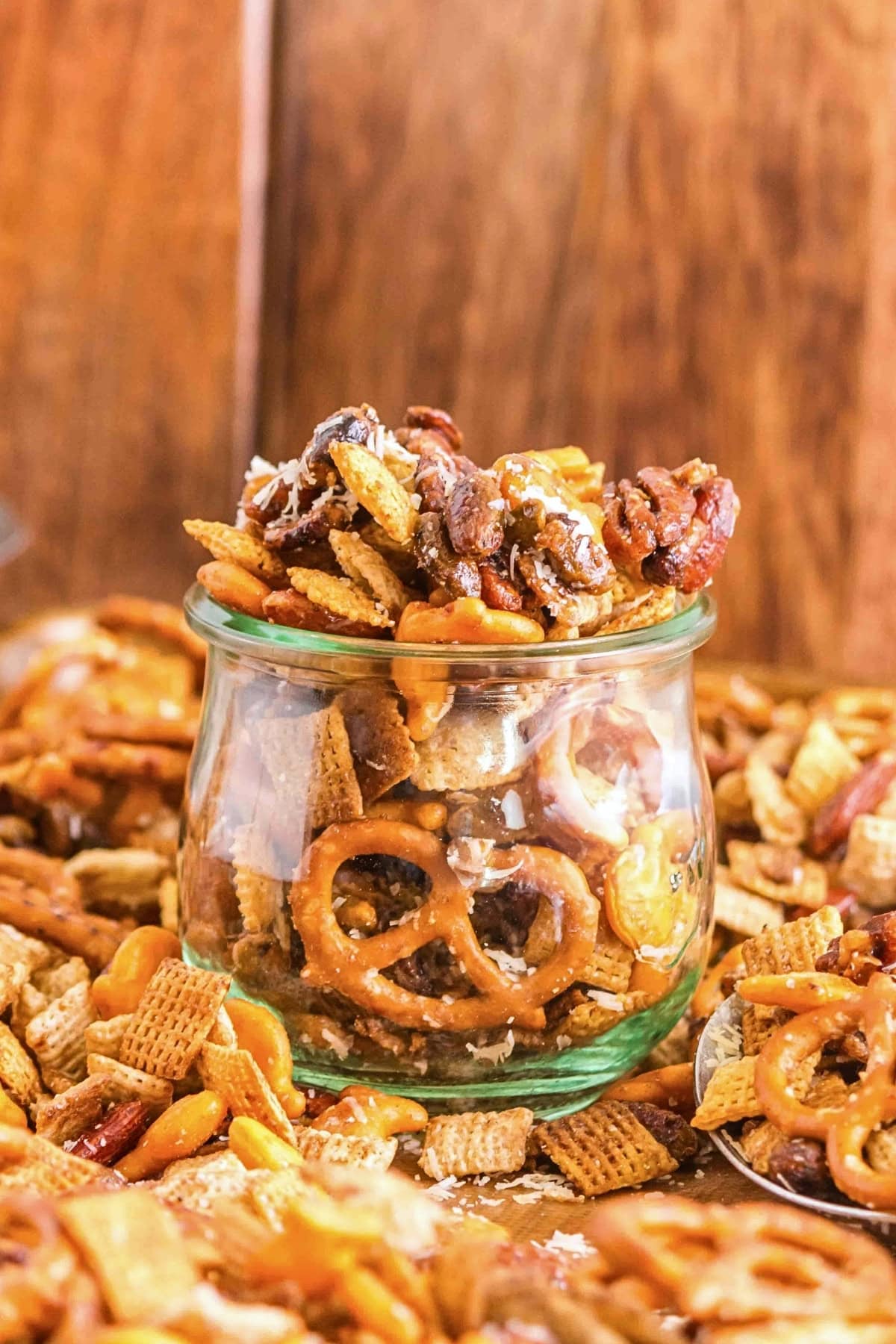 A glass jar filled with snack mix, including pretzels, nuts, and cereal pieces.