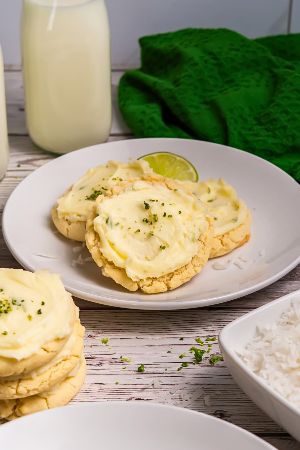 Frosted cookies with lime zest on a white plate, milk bottles in the background.