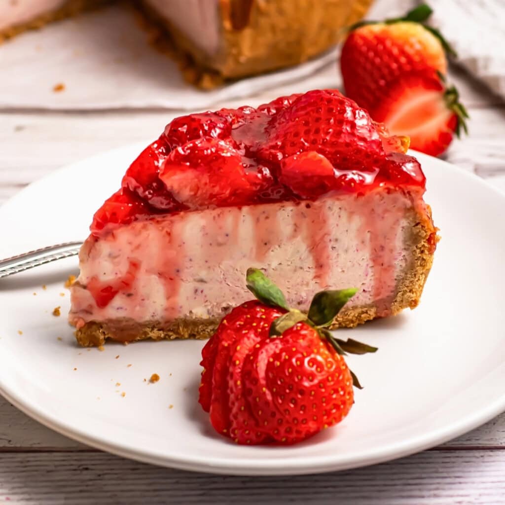 A slice of strawberry cheesecake with fresh strawberries on a white plate.