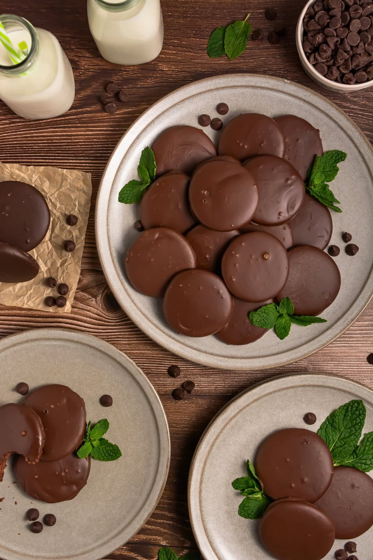 Chocolate-covered cookies on plates with fresh mint leaves and glasses of milk.