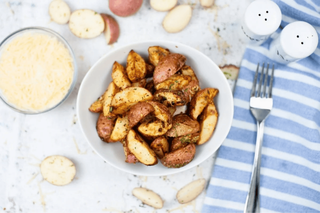 A bowl of seasoned roasted potato wedges with cheese and a fork nearby.