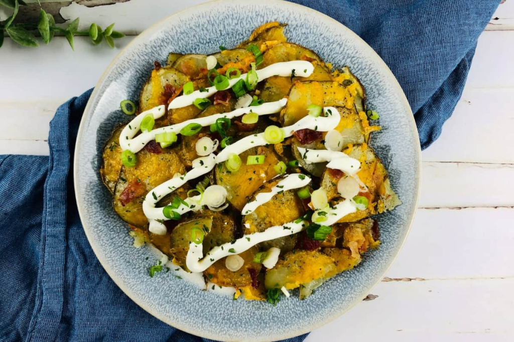 A bowl of loaded potato slices topped with melted cheese, sour cream, and green onions.