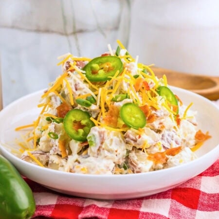 Potato salad with cheese, bacon, and sliced jalape&ntilde;os on a white plate.