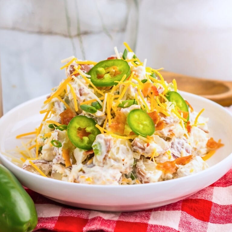 Potato salad with cheese, bacon, and sliced jalapeños on a white plate.