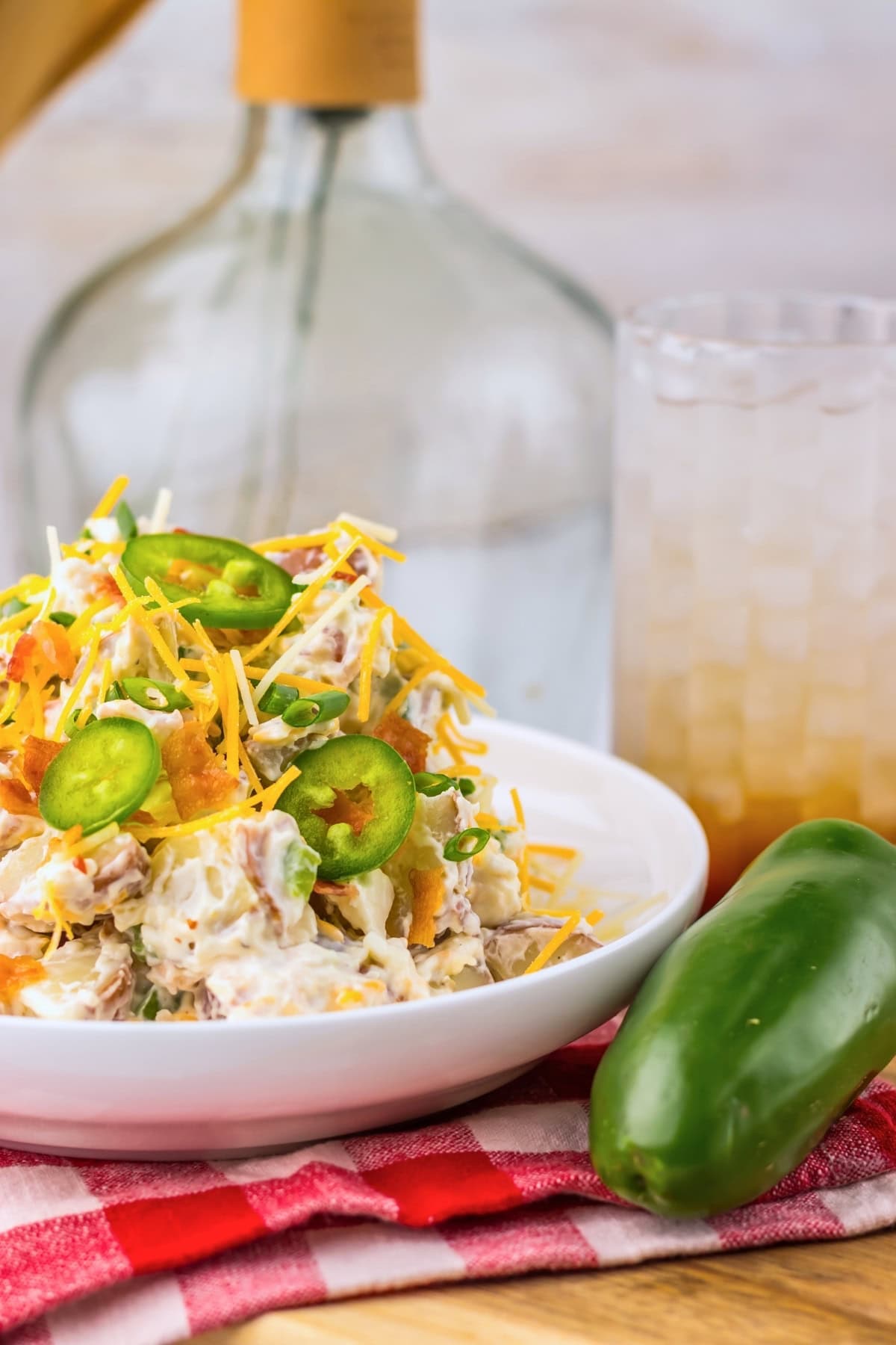 Bowl of potato salad with cheese and jalape&ntilde;os, drink and jalape&ntilde;o beside it.