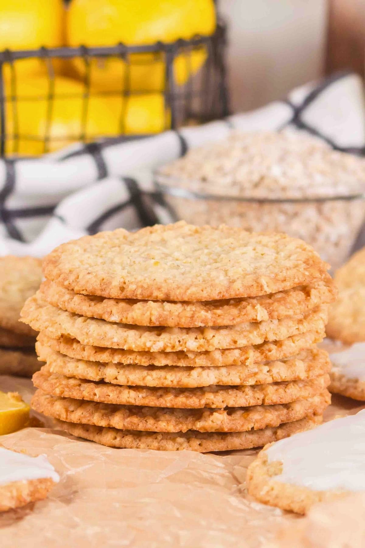 A stack of oatmeal cookies on parchment paper, with oats and lemons in the background.