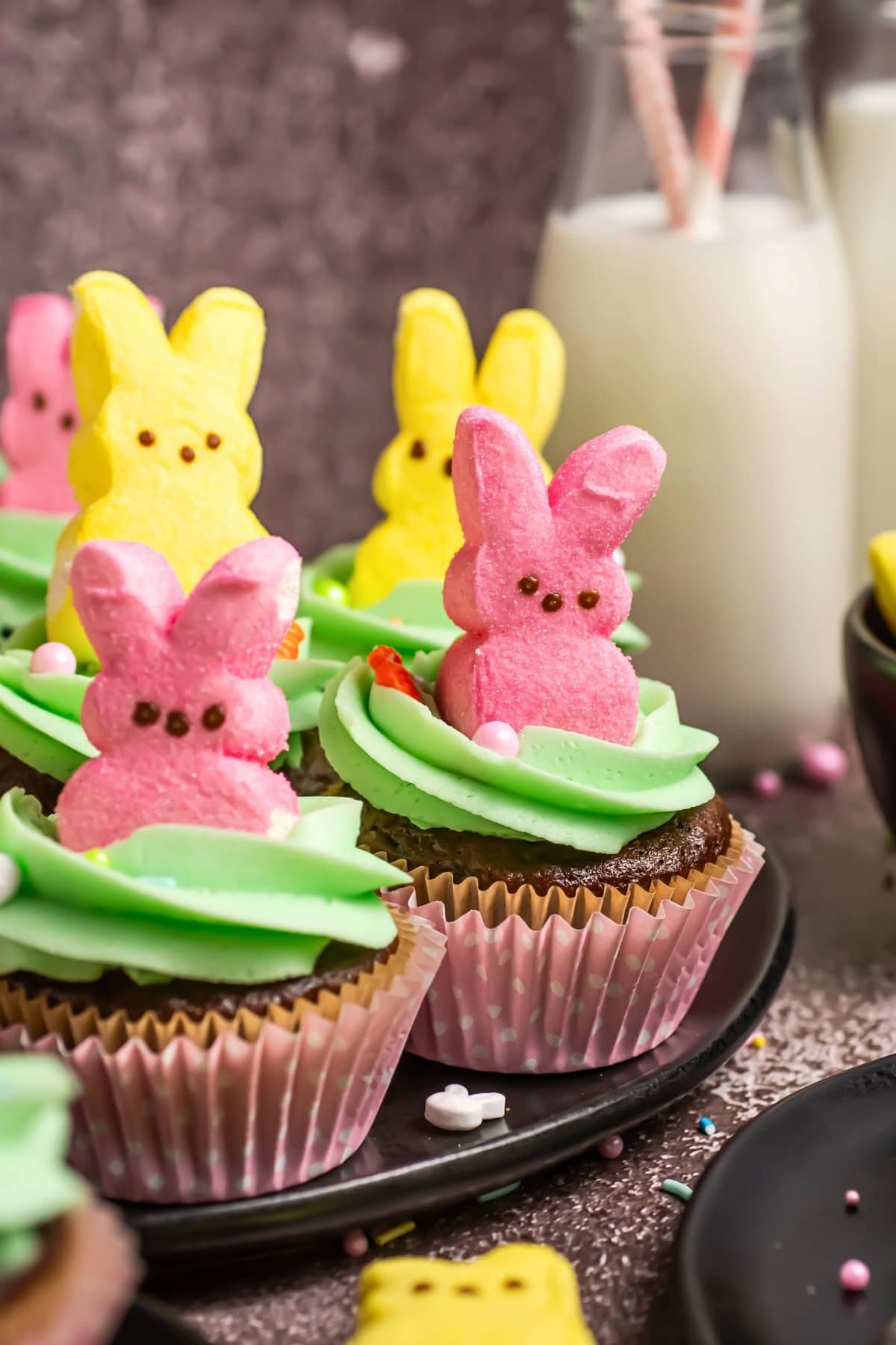 Chocolate cupcakes with pink and yellow bunny toppers and green icing.