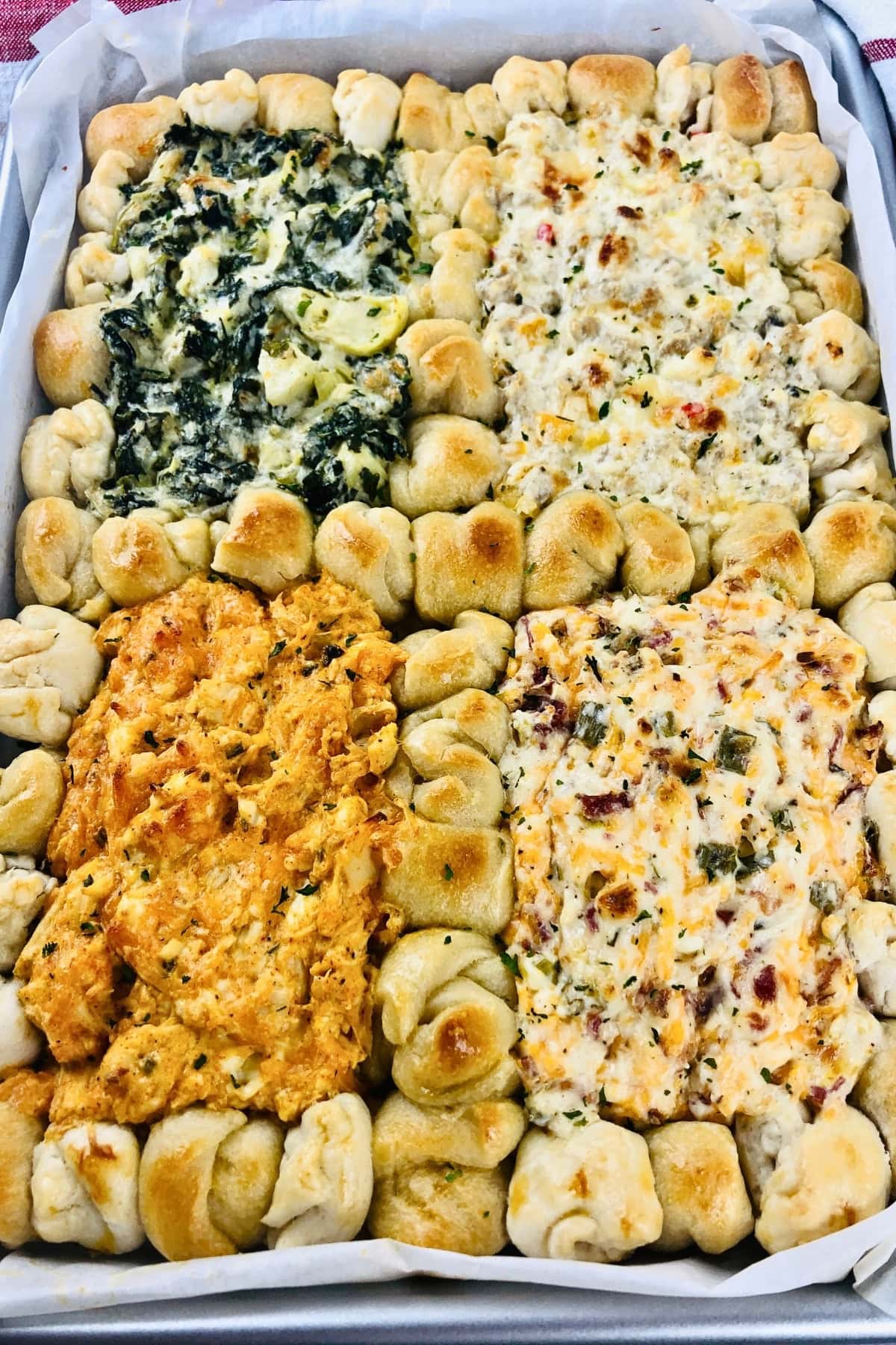 Four types of creamy dips surrounded by pull-apart bread in a baking dish.