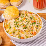 A bowl of creamy chicken stew with vegetables, served with a biscuit on top.