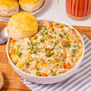 A bowl of creamy chicken stew with vegetables, served with a biscuit on top.