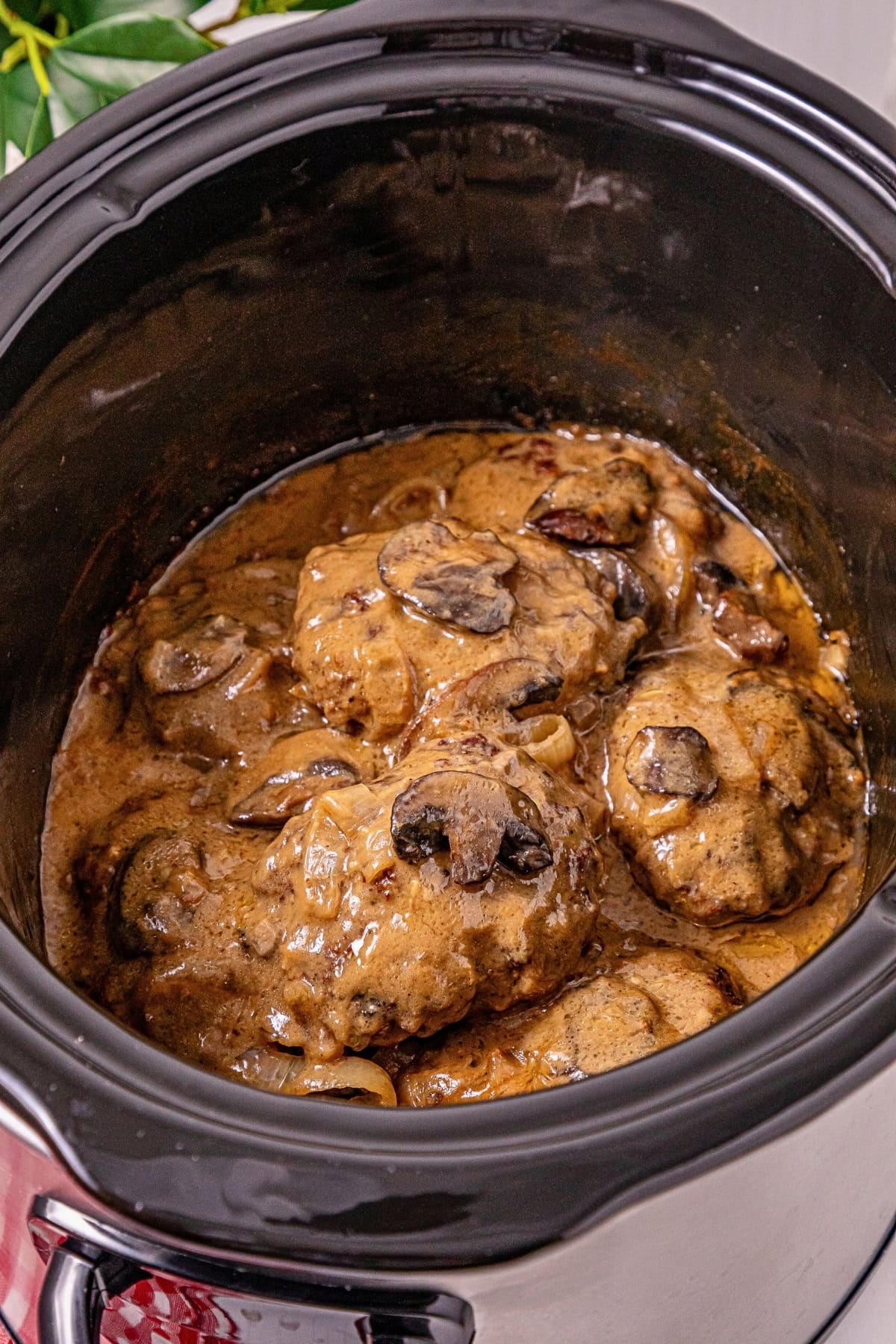 Salisbury steak with mushrooms and gravy cooking in a slow cooker.