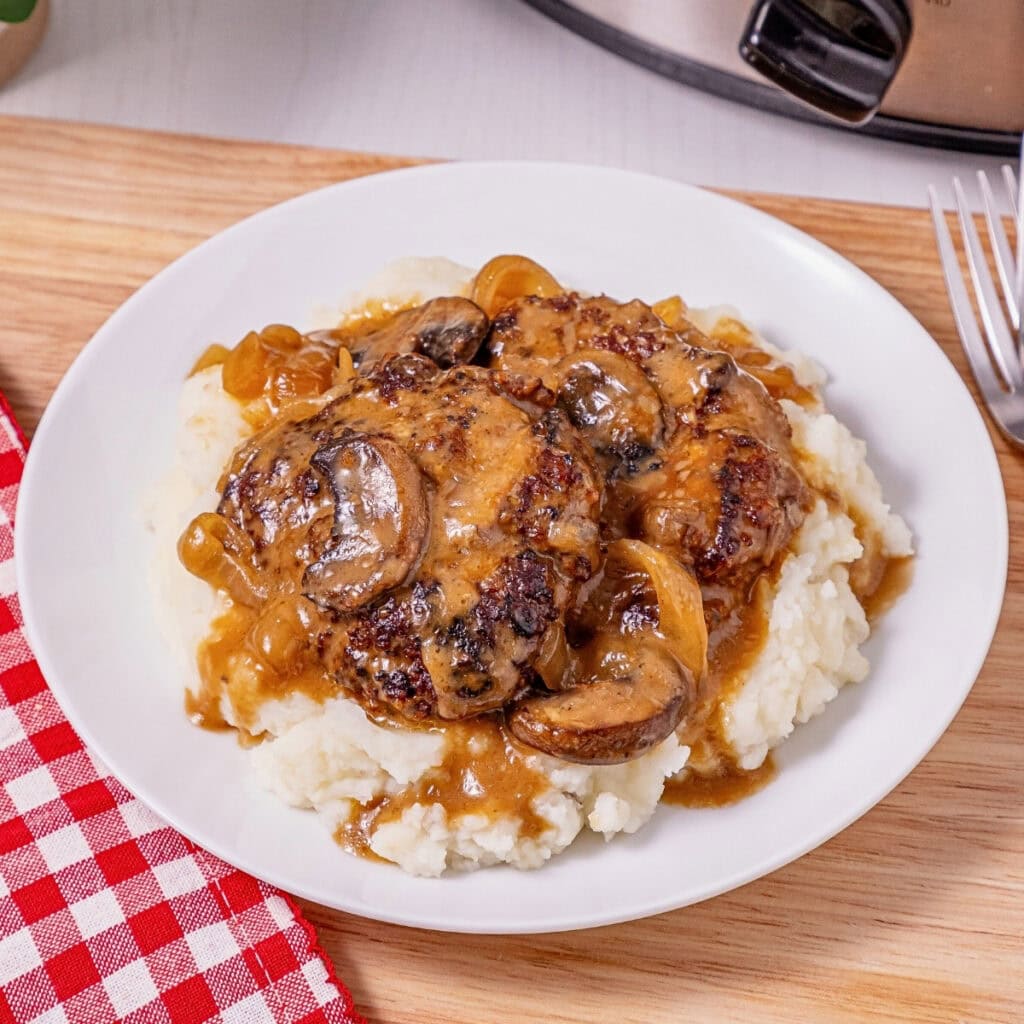 Salisbury steak with gravy, mushrooms, and onions over mashed potatoes on a plate.