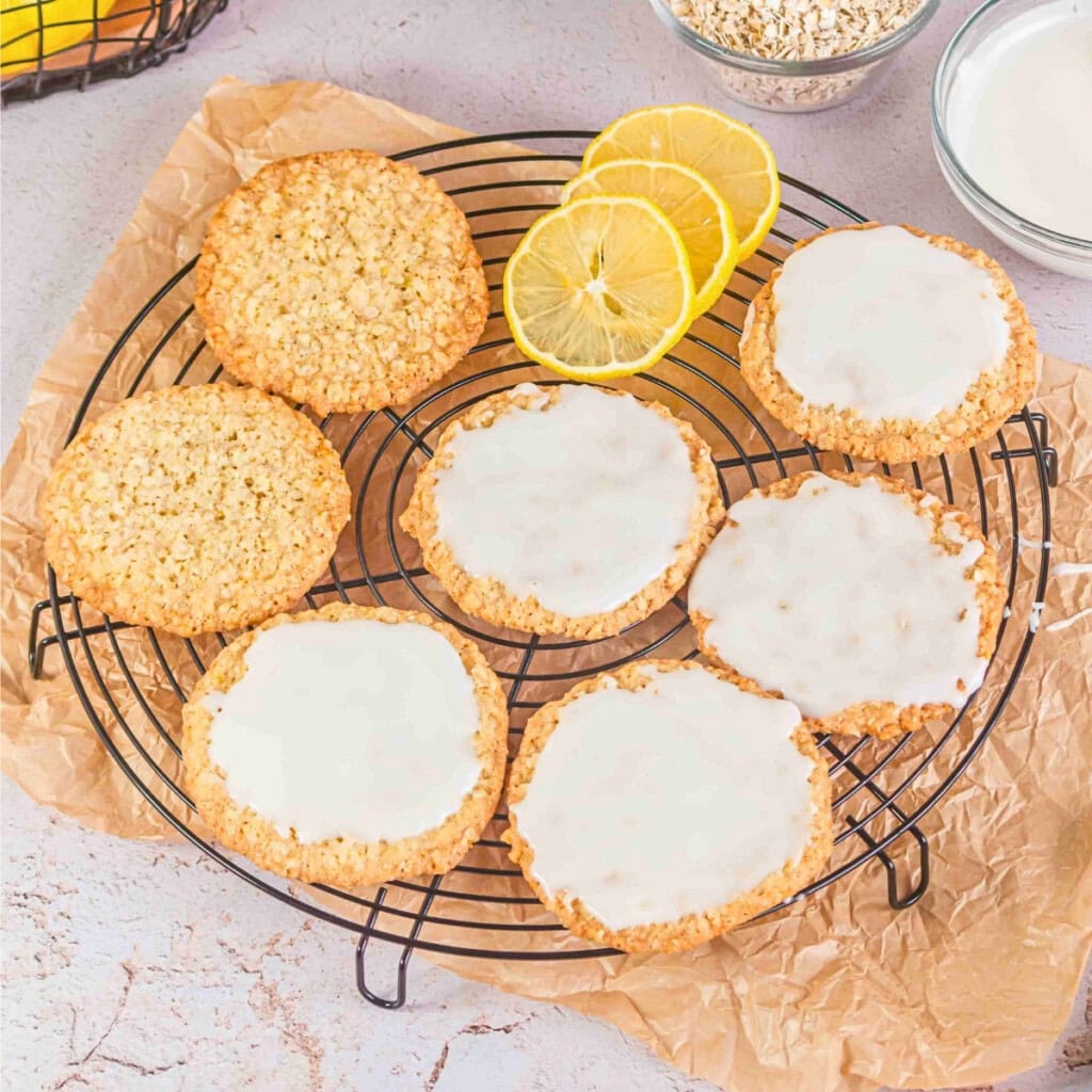 Oatmeal cookies with white icing on a wire rack, with lemon slices nearby.