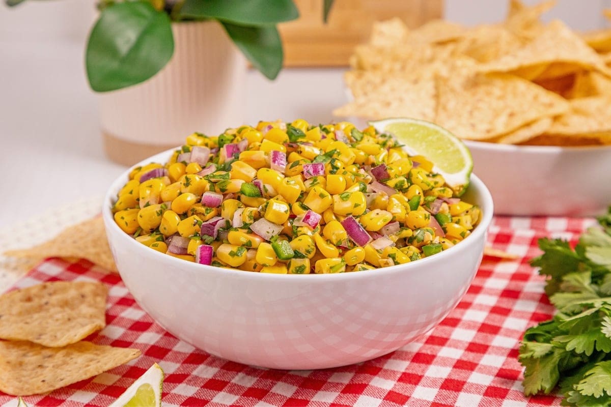 A bowl of corn salsa with red onion and herbs, next to tortilla chips.