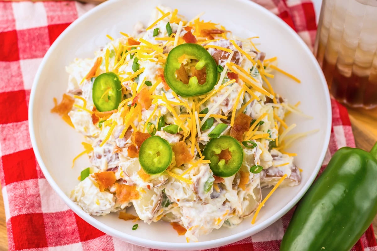 Potato salad topped with shredded cheese, bacon, jalape&ntilde;o slices, and green onions.