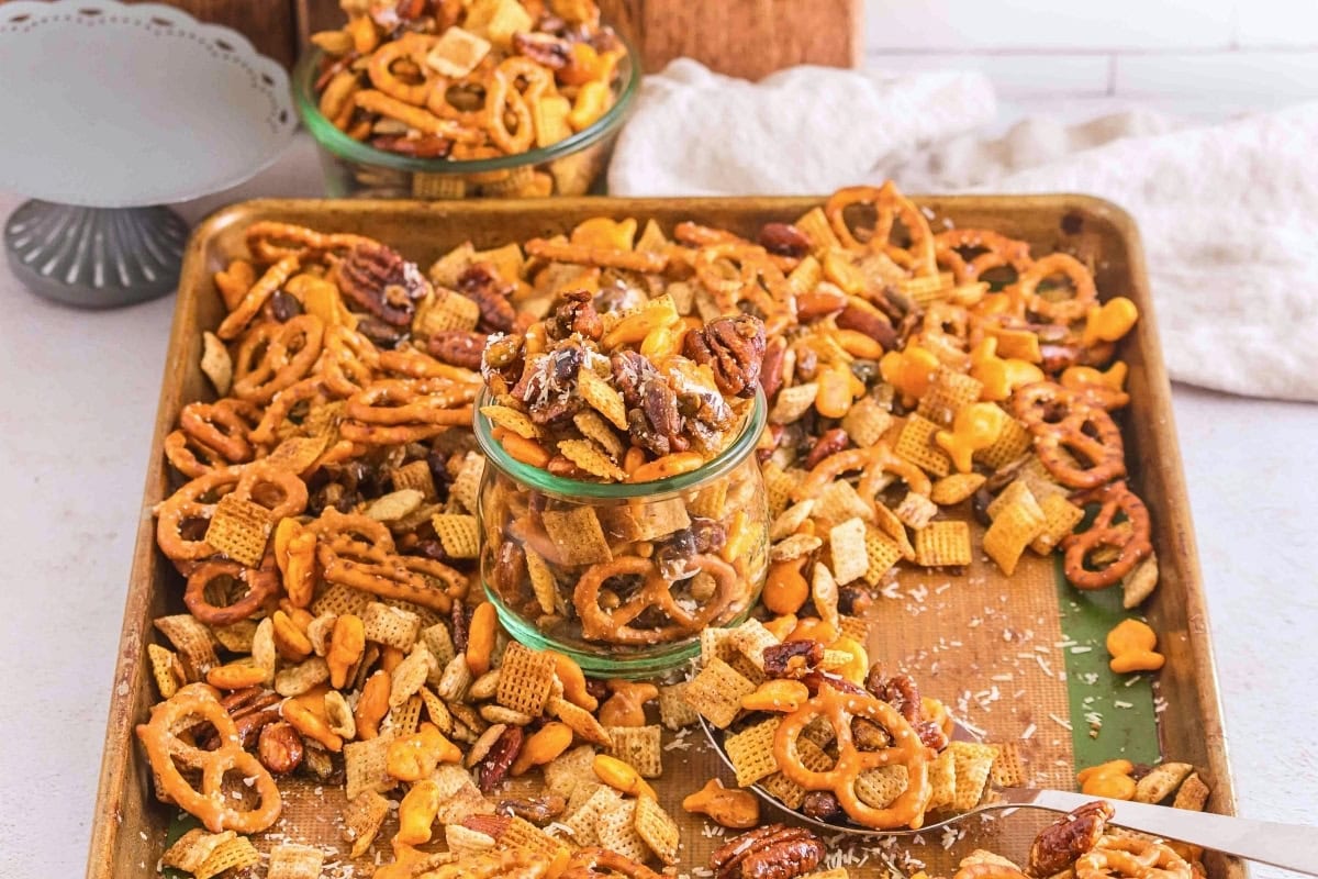 A baking sheet with mixed snack mix, including pretzels, nuts, and Chex cereal.