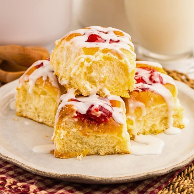 Four cherry sweet rolls with white icing are stacked on a plate.