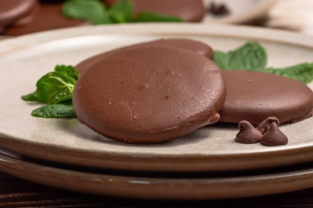 Chocolate-covered cookies on a plate with mint leaves and chocolate chips.