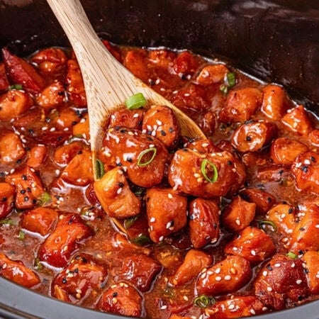 Wooden spoon scooping glazed chicken bites with sesame seeds and green onions.