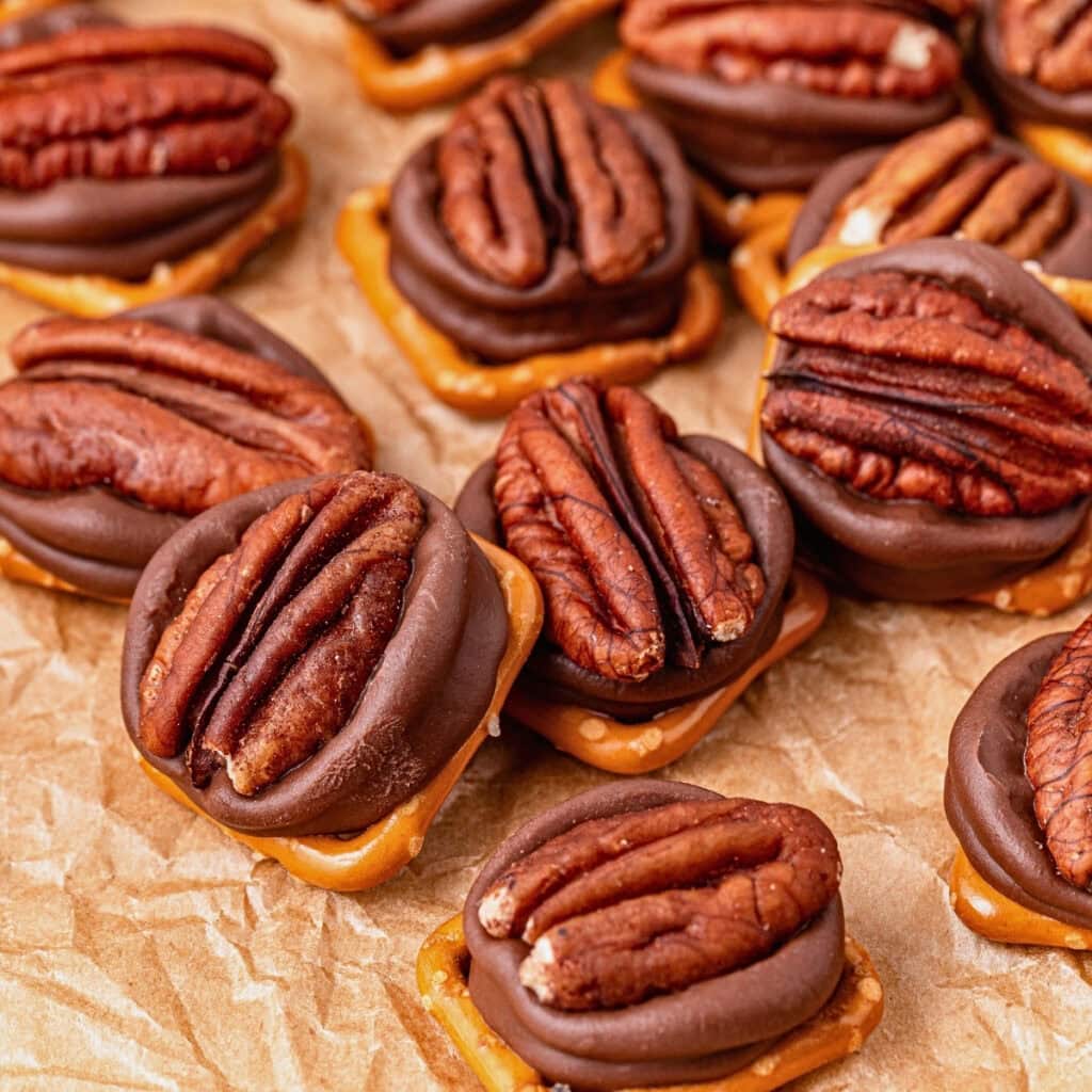 Pecans on chocolate and pretzel bites arranged on crinkled parchment paper.