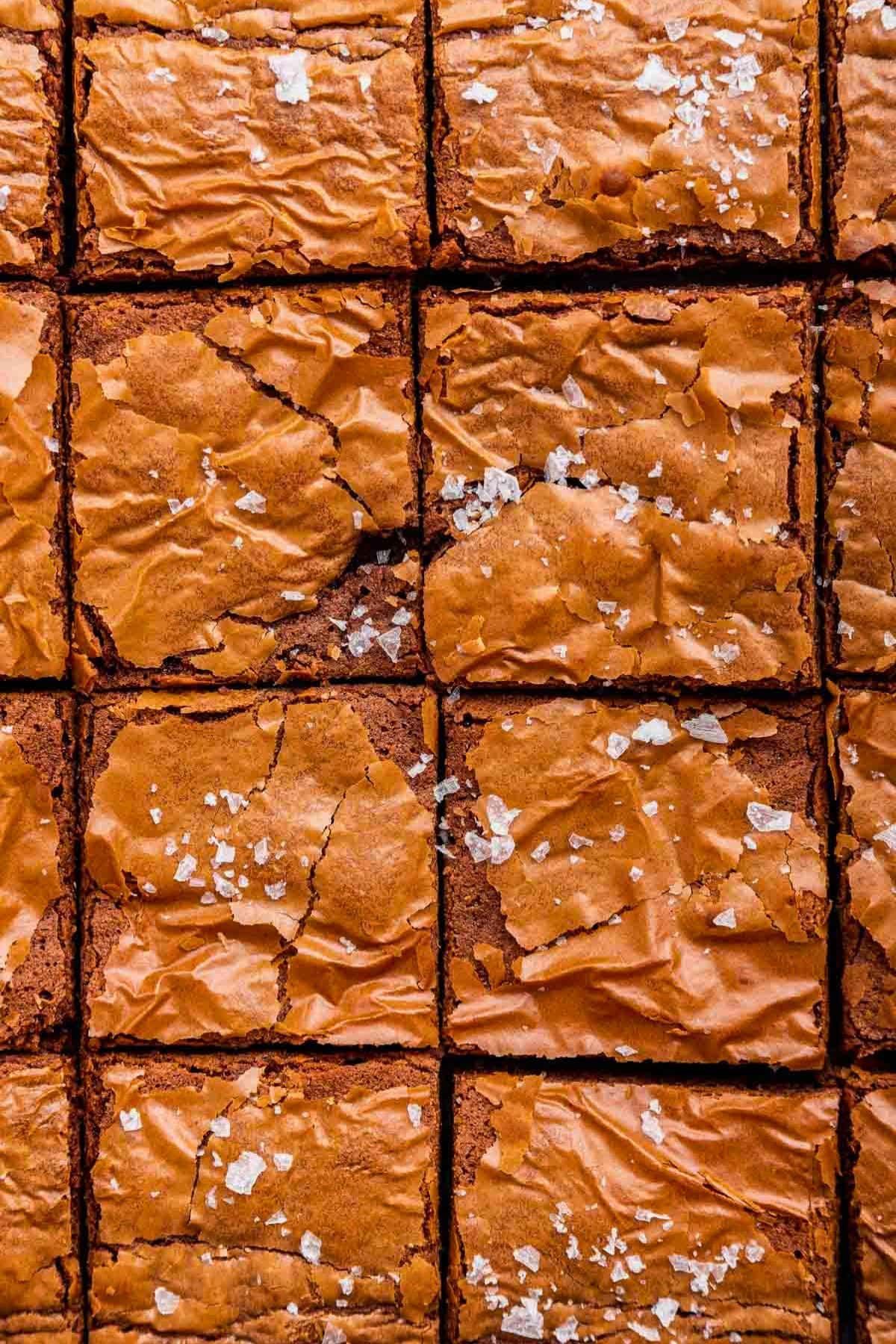 Close-up of sliced brownies with a flaky top, sprinkled with sea salt.