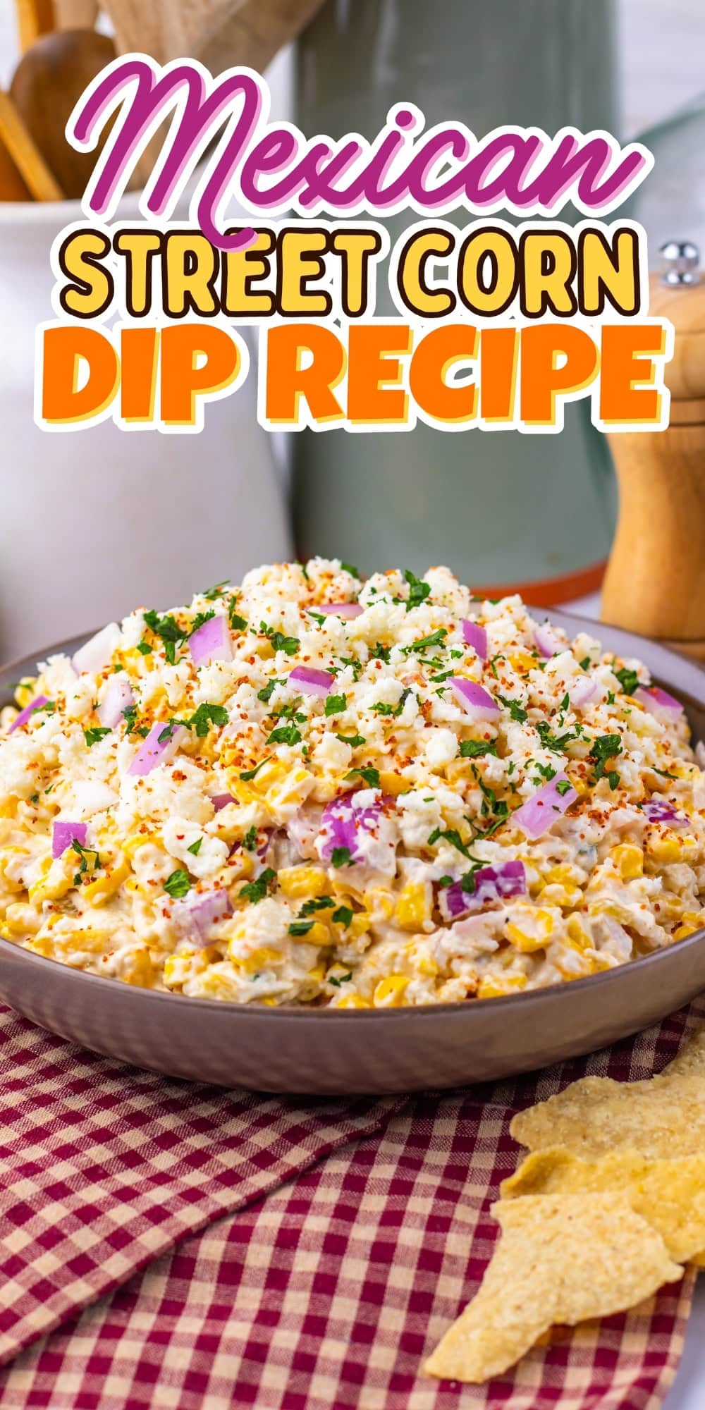 Bowl of Mexican street corn dip with tortilla chips on a red checkered cloth.