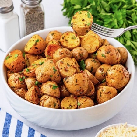 A bowl of seasoned roasted potatoes with herbs, with a fork lifting one piece.